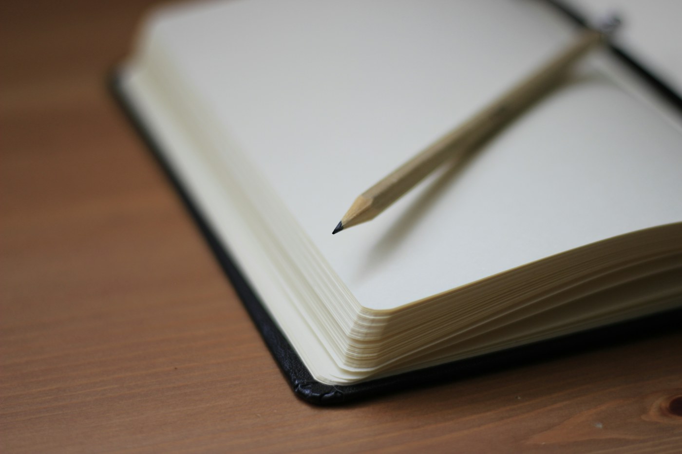 Wooden pencil resting on the blank pages of an open notebook on a wood desk.